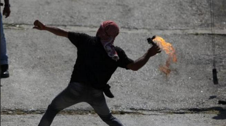 A Palestinian youth throws a Molotov cocktail towards Israeli soldiers close to the West Bank city of Ramallah (Illustrative)