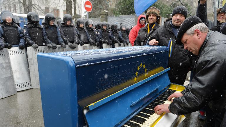 A man plays on a piano decorated as the EU flag in front of riot police as protesters picket Viktor Yanukovych's presidential office in Kiev on December 7, 2013