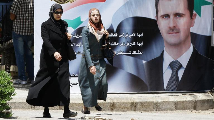 Two women walk past a huge billboard bearing a portrait of Syrian President Bashar al-Assad in the capital Damascus on May 27, 2014