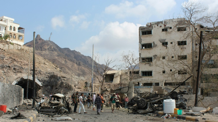 Armed Yemeni men look at the wreckage of a vehicle in the aftermath of a suicide car bombing on January 18, 2016 on the residence of Aden's police chief, General Shalal Shaea