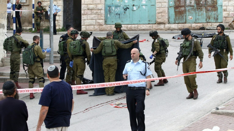 Israeli soldiers cover the body of a Palestinian who was reportedly killed by an Israeli soldier while he was down on March 24, 2016, in the district of Tal Rumeda in Hebron
