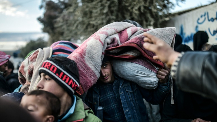 A man carrying belongings on his head looks on as Syrians fleeing the northern embattled city of Aleppo wait on February 5, 2016 in Bab-Al Salama, near Turkish crossing gate