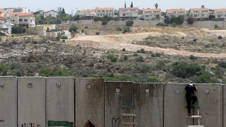 A Palestinian protester climbs Israel’s controversial separation barrier during clashes with Israeli security forces following a demonstration against Israeli settlements and its separation wall, in the West Bank village of Nilin