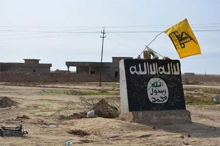 A flag of the Shiite Hezbollah militant group flutters over a mural depicting the emblem of the Islamic State (IS) group in Al-Alam village, northeast of the multi-ethnic Iraqi city of Tikrit in northern Iraq, on March 9, 2015 - Younis al-Bayati (AFP/File) Younis al-Bayati (AFP/File)