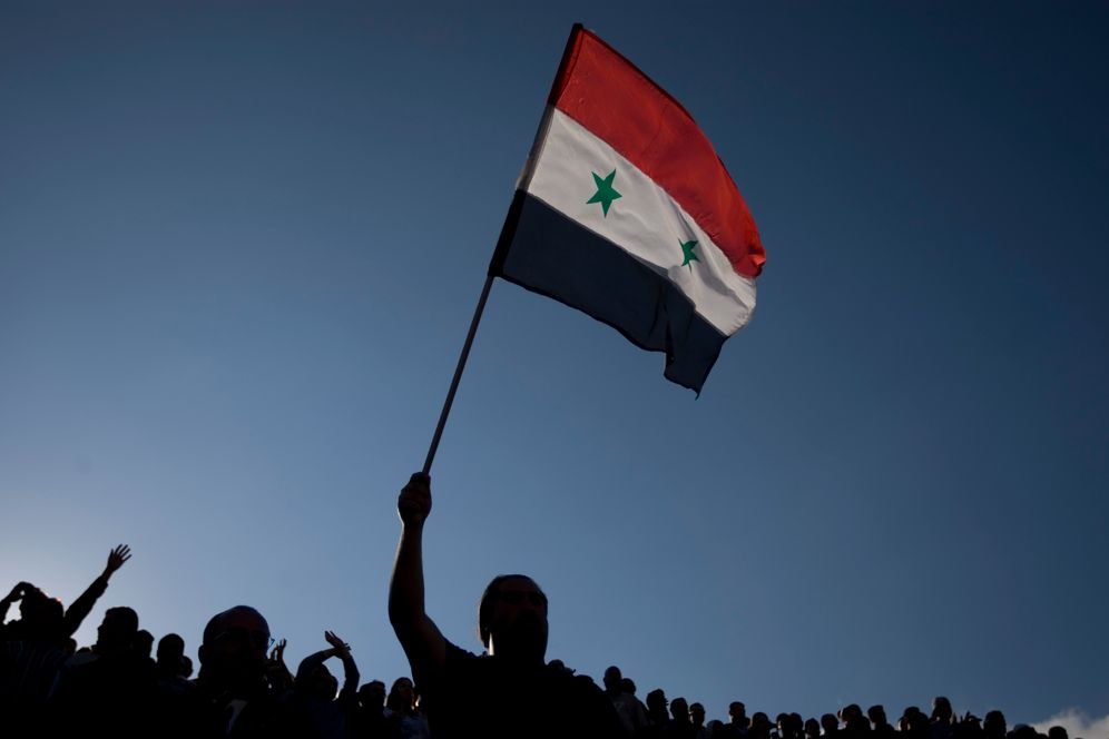 A Druze man waves a Syrian flag as they and others stand near the border fence between Israel and Syria as Syrian demonstrators marking the anniversary of the mass displacement of Palestinians surrounding Israel's establishment in 1948 leave the village o