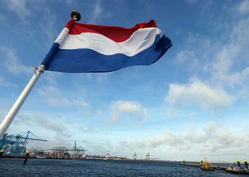 The Dutch flag flies on the stern of a ship as it passes a container terminal, rear, in the harbor of Rotterdam, Netherlands, Tuesday, Sept. 11, 2018