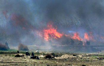Men believed to be Islamic State fighters walk amid flames and smoke in the jihadist group's last remaining position in the village of Baghouz on March 18, 2019