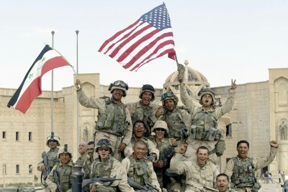 Des soldats américains brandissent les drapeaux américain et irakien devant le palais al-Faruq, à Tikrit, en Irak, le 14 avril 2003