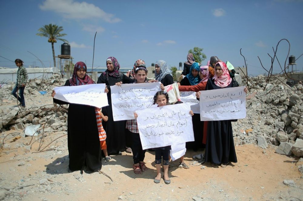 نسوة يرفعن لافتات وسط الدمار في الذكرى الاولى للحرب على غزة، في قرية خزاعة شرق خان يونس جنوب قطاع غزة في 7 تموز/يوليو 2015