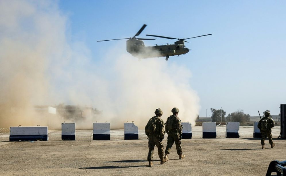US troops walk as a US Army C-47 Chinook helicopter flies over the village of Oreij, south of Mosul, on February 22, 2017, where a temporary military base has been established for an assault on the city's west bank