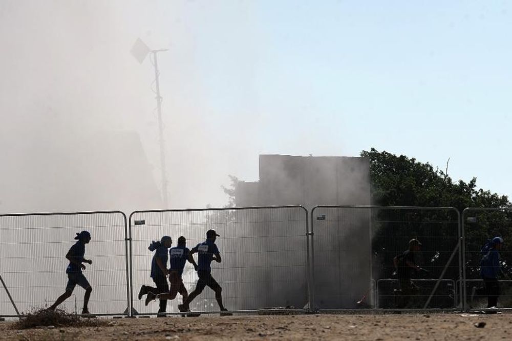Israelis run for cover seconds after an Iron Dome system (background) fired an anti-rocket missile near the city of Ashkelon on August 26, 2014