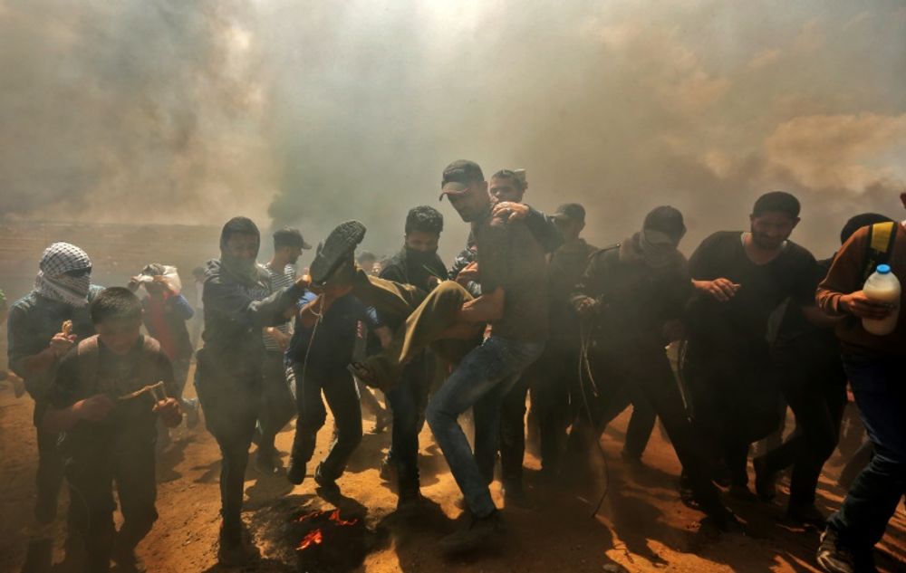 Palestinians carry a demonstrator injured during clashes with Israeli forces near the Gaza Strip border on May 14, 2018