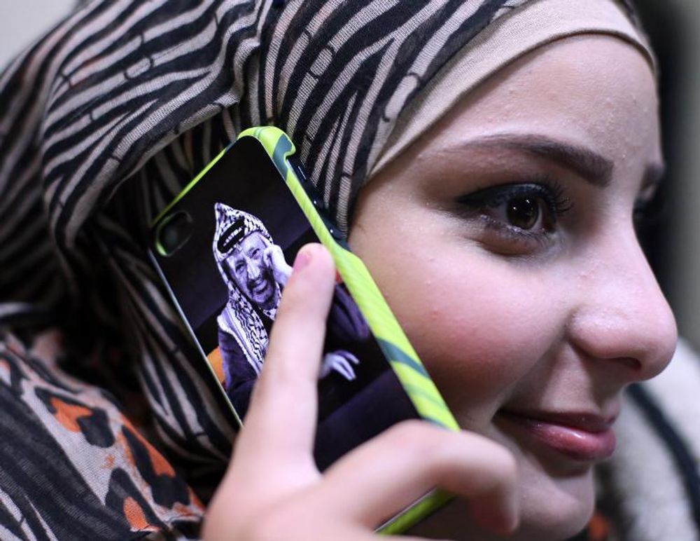 A Palestinian woman uses a mobile phone bearing a portrait of late Palestinian leader Yasser Arafat on November 5, 2014, in the West Bank city of Ramallah