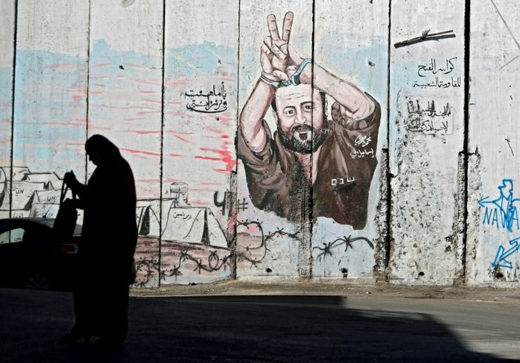 A woman walks past graffiti depicting Israel's most famous Palestinian prisoner, Marwan Barghouti, who is revered by Palestinians but reviled by many Israelis for his role in the second Palestinian intifada of 2002-5 that earnt him five life terms