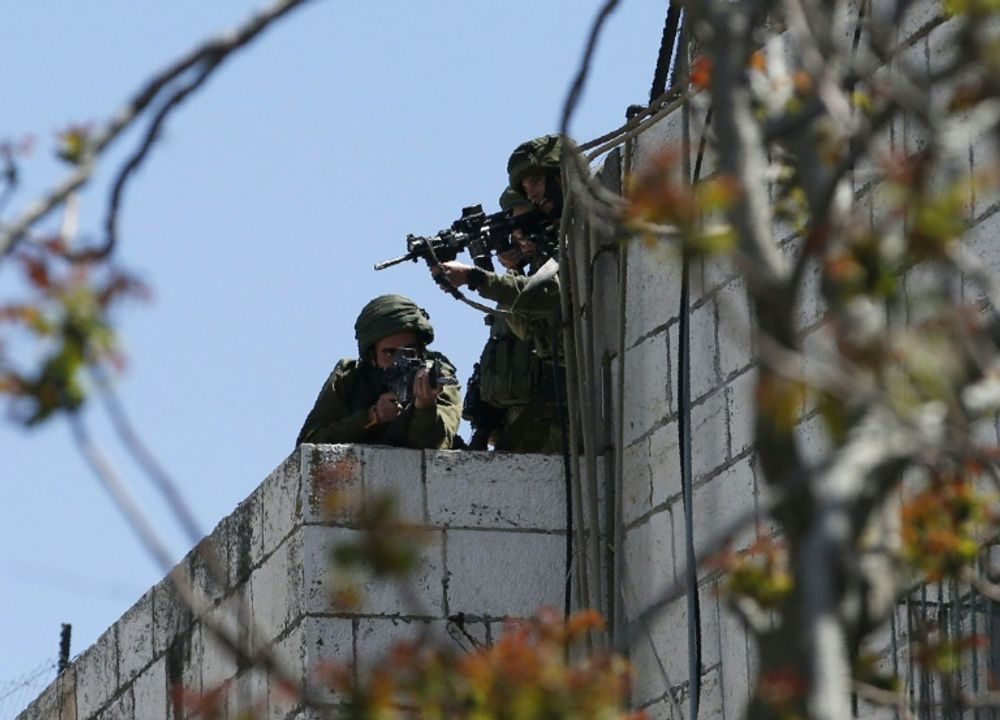 Israeli forces aim their weapons towards Palestinian demonstrators on March 31, 2018 during clashes in occupied West Bank city of Hebron