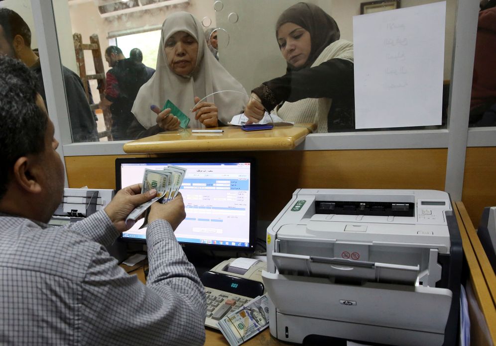 FILE- A Palestinian Hamas government employee signs to receive 50 percent of her long-overdue salary donated by Qatar, while others wait in the queue, at the main Gaza Post Office, in Gaza City, Friday, Dec. 7, 2018.
