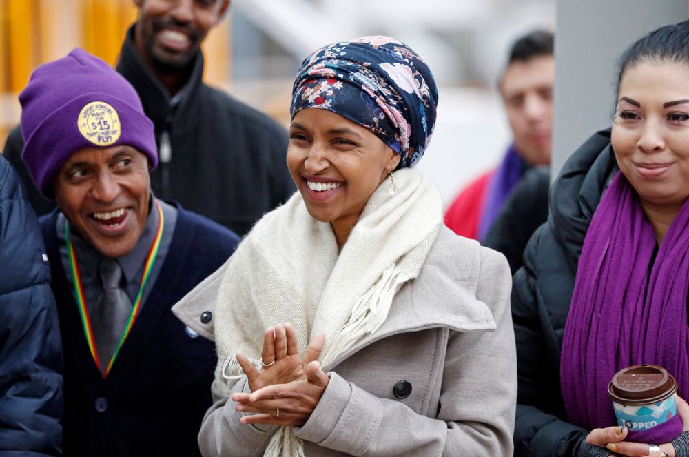 Ilhan Omar, center, the first Somali-American elected to a state legislature, applauds during a rally Tuesday, Nov. 29, 2016, at the Minneapolis-St. Paul International Airport in Minneapolis, in support of efforts calling for $15 minimum wages. Those in a