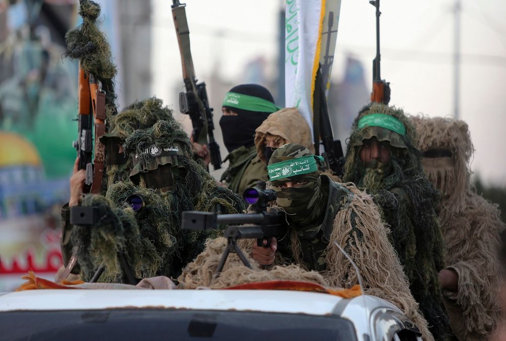 Palestinian masked members from the Izzedine al-Qassam Brigades, a military wing of Hamas, wear camouflage while sitting behind a sniper gun during a rally along the streets of Rafah refugee camp, Gaza Strip, Sunday, Aug. 21, 2016. The Arabic on their hea