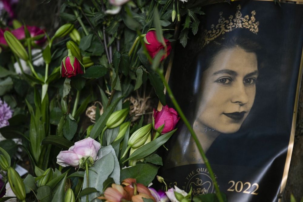 A portrait of Britain's Queen Elizabeth II is seen next to flowers placed outside of Buckingham Palace in London, UK, on September 11, 2022.
