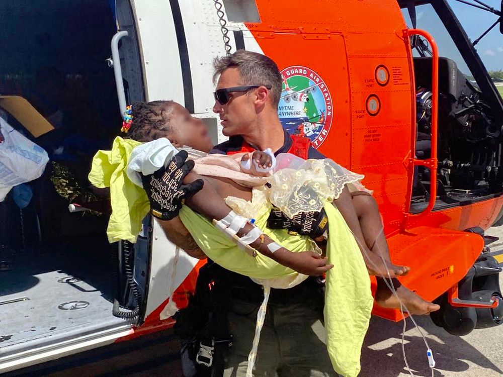 Un membre de l'équipage aérien de la Garde côtière aide à transporter un enfant grièvement blessé à Port-au-Prince, Haïti, le 15 août 2021