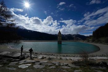 Two visitors stand near the Resia lake in Curon Venosta, northern Italy.
