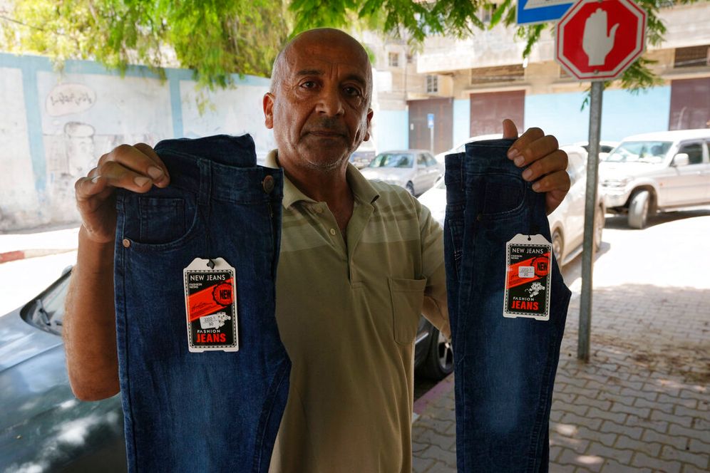 A Gaza clothes merchant holds up jeans during a sit-in to protest a new tax on imported goods, in front of the Clothes Traders Syndicate in Gaza City, July 21, 2022.
