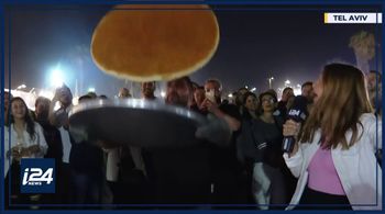 Natasha Kirtchuk, (R), reporter with i24NEWS, get an up-close look at a knafeh flipping at the Eat Tel Aviv food festival, Tel Aviv, May 23, 2022.