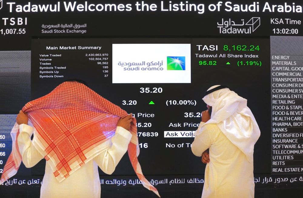 Saudi stock market officials watch the stock market screen displaying Saudi Arabia's state-owned oil company Aramco in Riyadh, Saudi Arabia.
