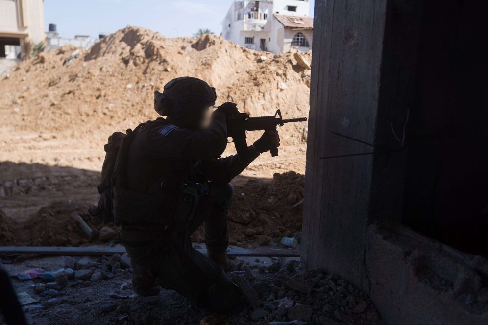 IDF spokesperson's unit Israeli soldier kneels with his weapon, taking cover from the corner of a building in Gaza