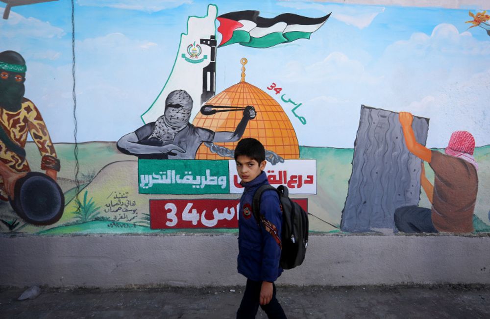 A child walks past a large mural depicting soldiers of Qassam, the military wing of Hamas, in Khan Yunis, Gaza Strip, on December 11, 2021.