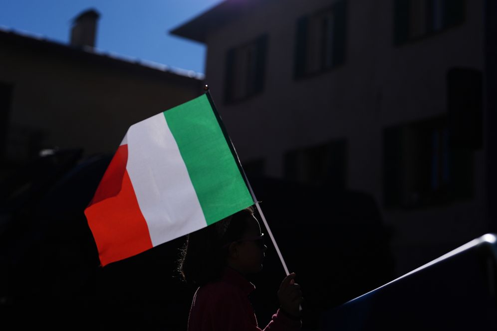 A girl holds an Italian flag as she watches Italian athletes compete in an alpine ski women's giant slalom race on a big screen in Piazza Cavour at the 2026 Winter Olympics in Bormio, Italy, Sunday, Feb. 15, 2026. (AP Photo/Rebecca Blackwell)
