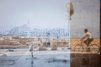 A man riding his bicycle is reflected on an old picture of Jaffa displayed in a window, in the Jaffa neighborhood of Tel Aviv, Israel.