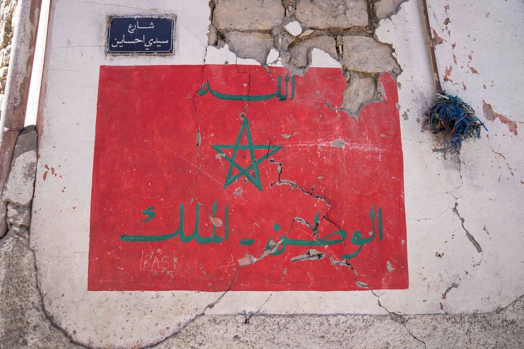 جدار متصدع يظهر عليه علم المغرب ونقش باللغة العربية نصه: 