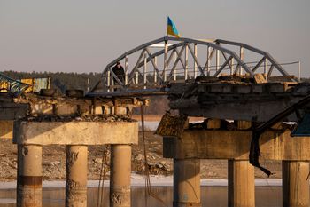 A man crosses a makeshift pedestrian bridge connecting the two sides of a destroyed road bridge in Staryi Saltiv, Ukraine.