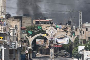 Smoke billows behind buildings and above an Israeli military armored vehicle during an operation in Jenin city, in the West Bank.