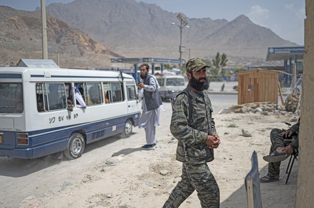 Taliban fighters stand guard as bus transports Afghan internally displaced to their homes to the east, at the United Nations High Commissioner for Refugees camp in the outskirts of Kabul, Afghanistan, on July 28, 2022.