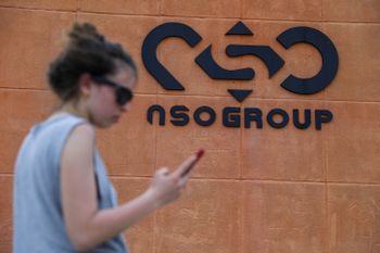 A woman standing with her phone next to the NSO Group company logo, outside the NSO Group offices in Sapir, southern Israel, on April 2, 2022.