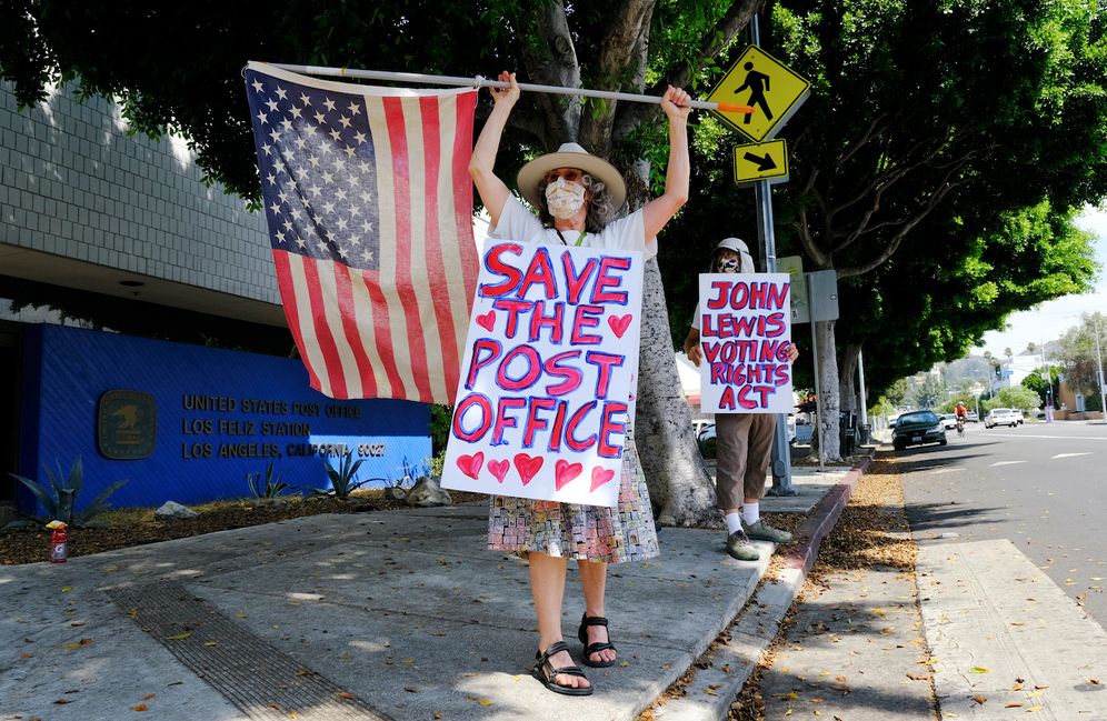 Erica Koesler, left, and David Haerle, both of Los Angeles, demonstrate outside a USPS post office, Saturday, Aug. 15, 2020, in the Los Feliz section of Los Angeles.