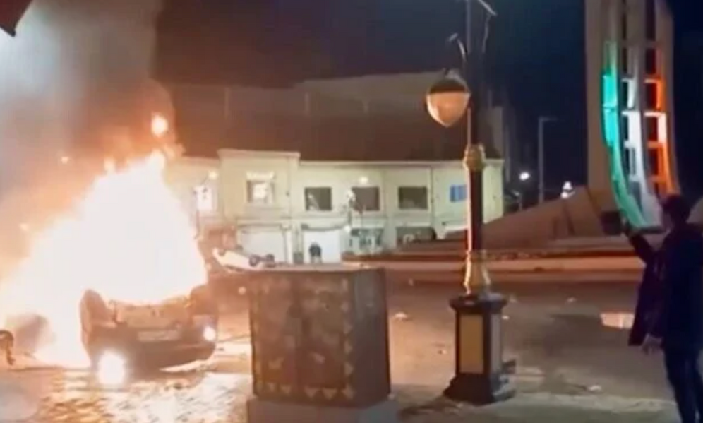 Cette image tirée d'une vidéo diffusée le 9 janvier 2026 par la télévision d'État iranienne montre un homme tenant un appareil pour filmer des véhicules en feu lors d'une nuit de manifestations massives à Zanjan, en Iran. 