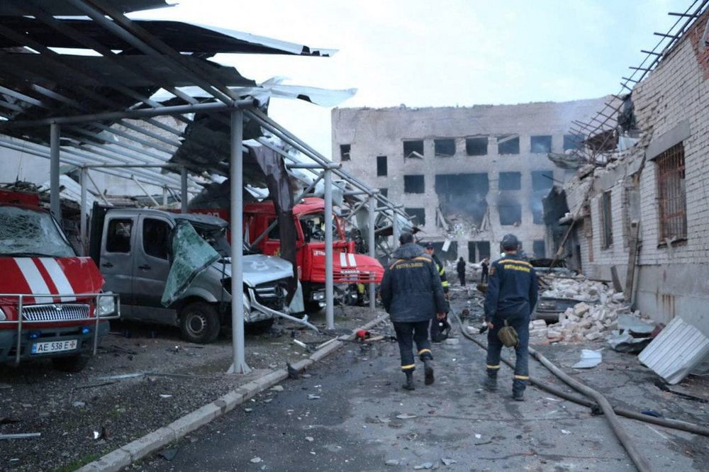Ukrainian rescuers walking past damaged emergency service trucks next to a damaged fire station after a strike in the Ukrainian city of Dnipro.
