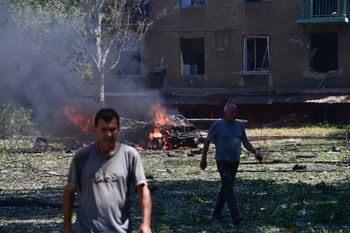 Civilians walk past a burning car as they leave after an air strike in the courtyard of hotel Industria and civilian residences in the center of Kramatorsk, Ukraine, on July 7, 2022