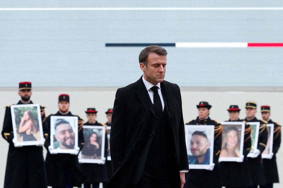 French President Emmanuel Macron walks past French Republican Guards who hold portraits of the French victims of the October 7 Hamas' attack, during a ceremony at the Invalides monument, February 7, 2024.