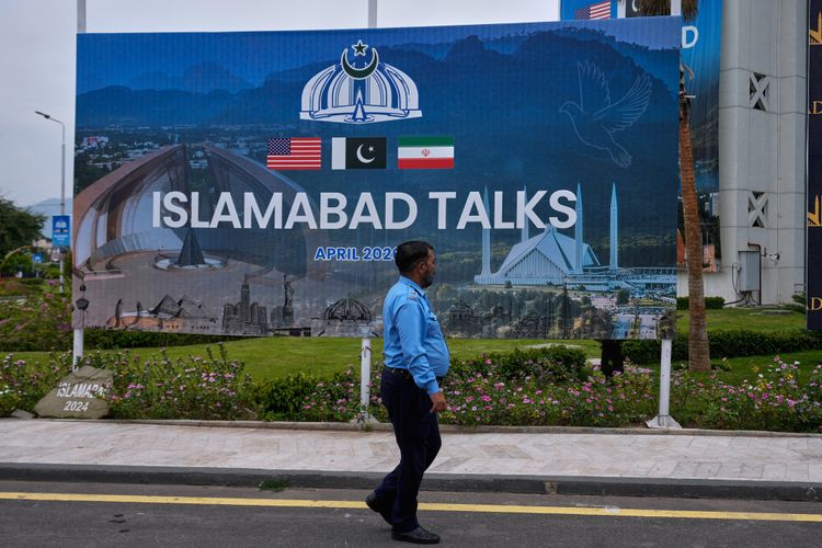 A police officer walks past a billboard regarding U.S. and Iran negotiations, outside a media facilitation center in Islamabad, Pakistan, Saturday, April 11, 2026