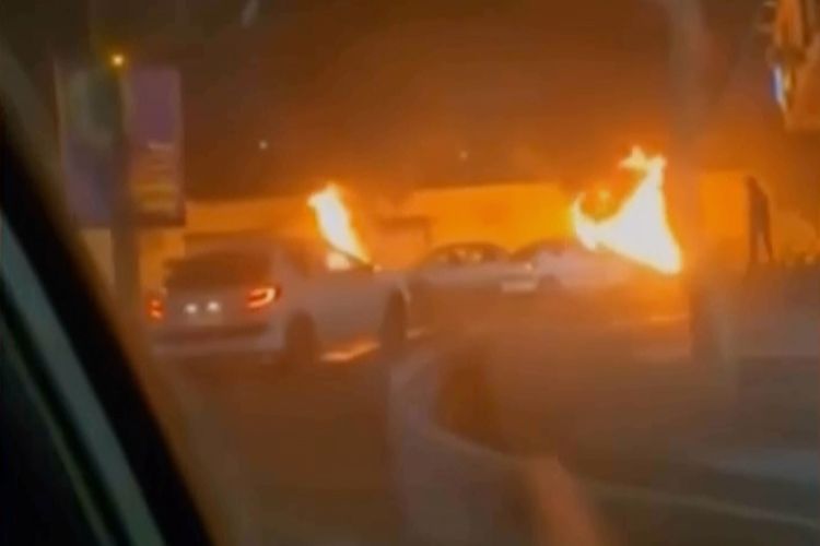 This frame grab from a video released Friday, Jan. 9, 2026, by Iranian state television shows cars driving past burning vehicles during a night of mass protests in Tehran, Iran. 