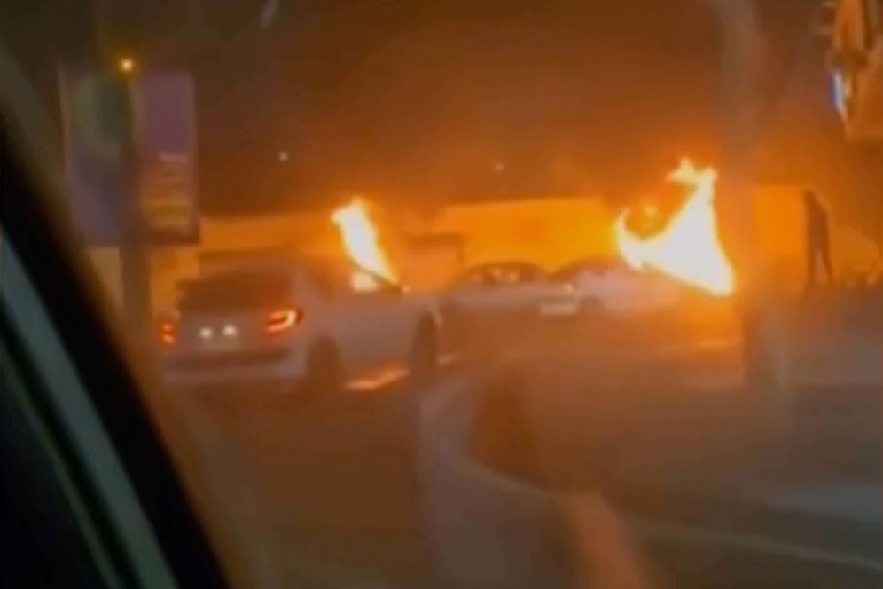 (Iranian state TV via AP) This frame grab from a video released Friday, Jan. 9, 2026, by Iranian state television shows cars driving past burning vehicles during a night of mass protests in Tehran, Iran.