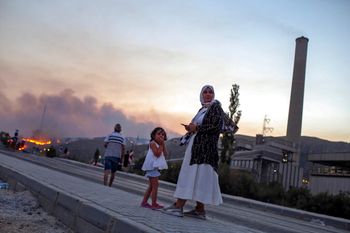 People stand in front of Kemerkoy Thermal Power Plant, right, as a wildfire approaches in the background, in Milas, Mugla, Turkey, August 3, 2021.