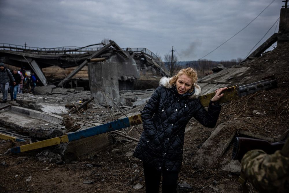 Une civile ukrainienne fait une pause après avoir traversé un pont détruit alors qu'elle évacue de la ville d'Irpin, au nord-ouest de Kiev en Ukraine le 7 mars 2022