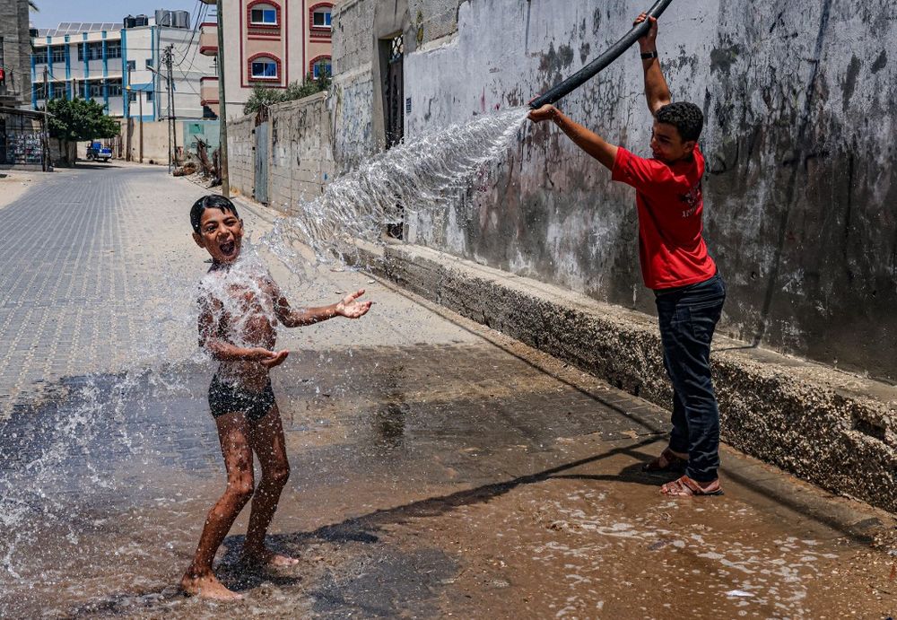 A Palestinian boy sprays a friend with water from a pipe, on a very hot day in the town of Rafah, in the southern Gaza Strip, on August 7, 2021.