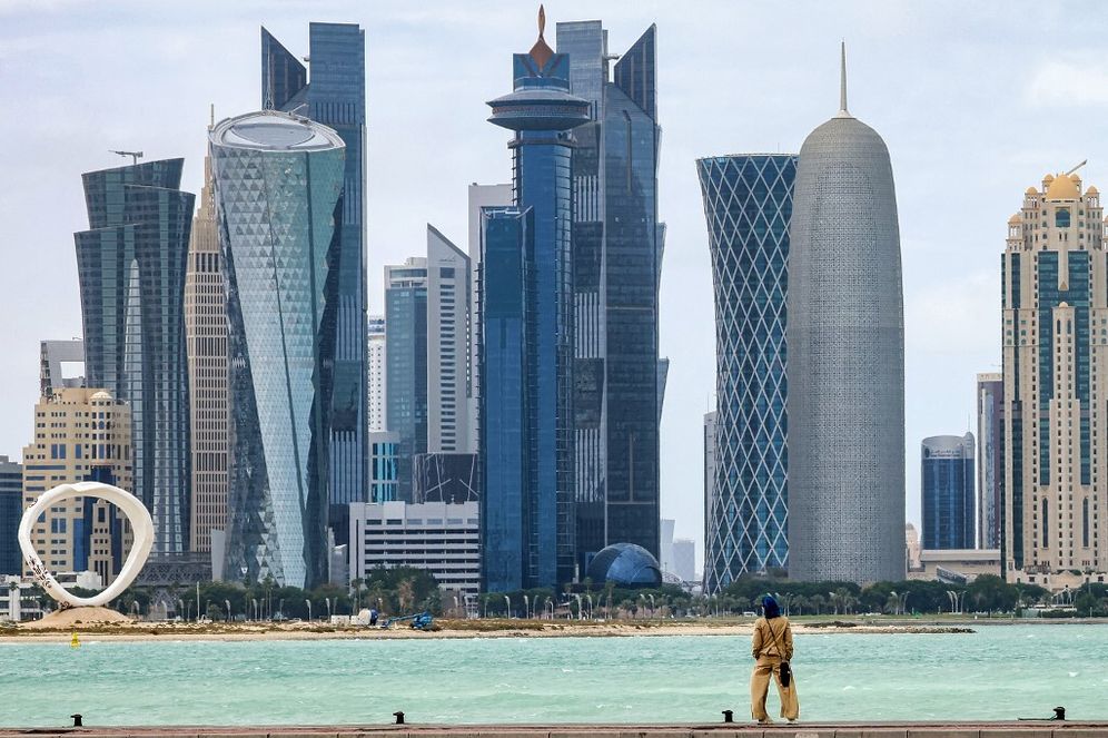 A woman stands at the water's edge on Doha's Corniche facing the skyscrapers of the West Bay district on April 16, 2024.