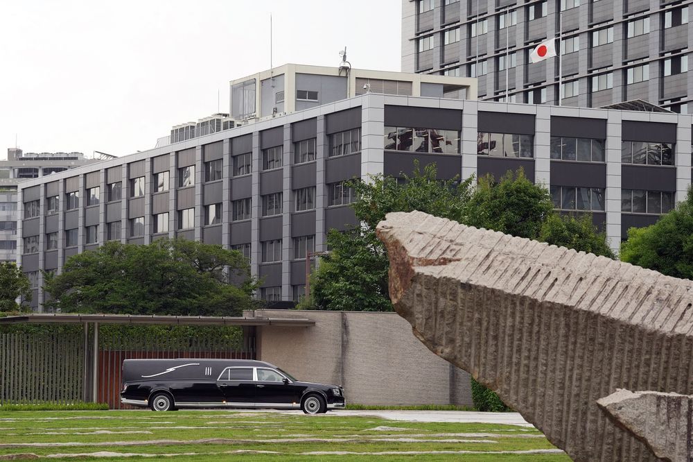 A hearse transporting the body of former prime minister Shinzo Abe makes a brief visit to the Prime Minister's Office after the funeral ceremony, as a Japanese flag (top R) flies as half-mast, in Tokyo on July 12, 2022.